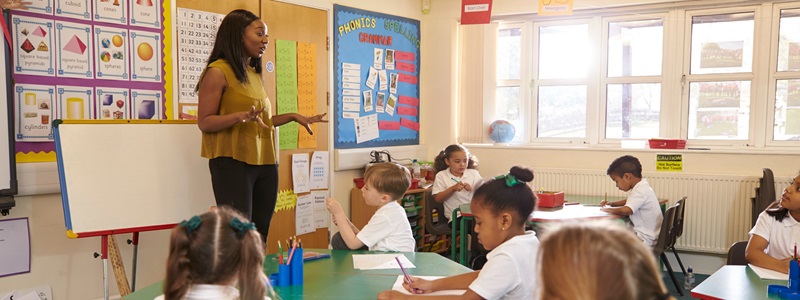 A teacher talking at the front of a classroom full of students during a lesson